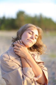 Closeup caucasian woman standing on beach and enjoying with sun rays. Concept of autumn photo session and resting outside.