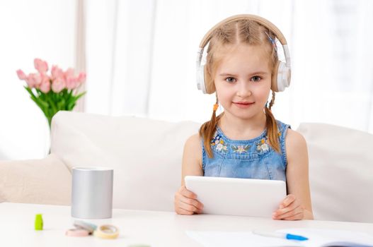 Beatiful little girl with white tablet with headphones on, in the room