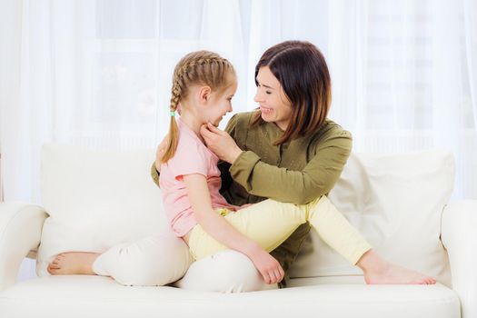 Funny mom and teenage little girl relaxing on the white couch