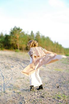 Young woman turning around on sand and wearing coat with white dress. Concept of happiness, summer vacations and fashion.
