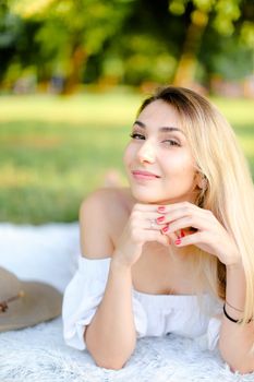 Young girl with red nails lying in park on plaid. Concept of having free time, picnic and summer vacations.