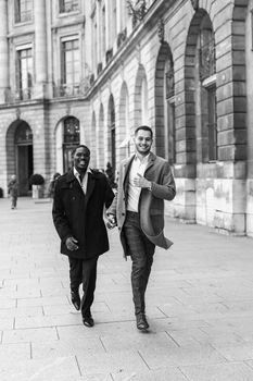 Black and white bw portrait in Paris. Caucasian man running with afroamerican male person and holding hands in city. Concept of happy gays and strolling.