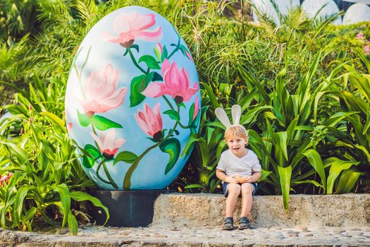 Cute little kid boy with bunny ears having fun with traditional Easter eggs hunt, outdoors. Celebrating Easter holiday. Toddler finding, colorful eggs.