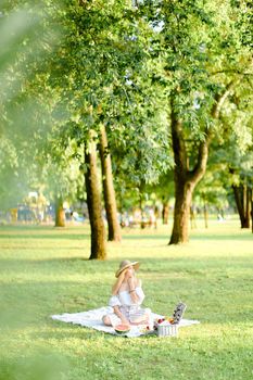 Young caucasian woman in hat resting on plaid with fruits in garden. Concept of summer picnic in park, nature and free time.