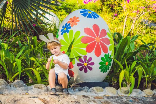 Cute little kid boy with bunny ears having fun with traditional Easter eggs hunt, outdoors. Celebrating Easter holiday. Toddler finding, colorful eggs.