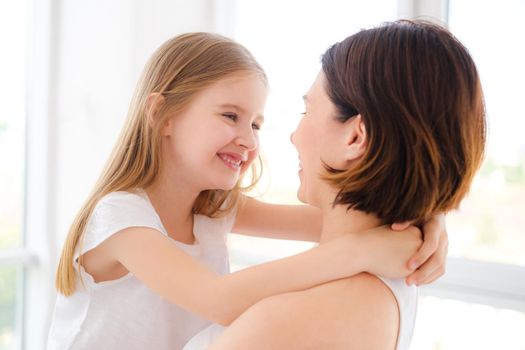 Mother with her little daughter girl hugging in white room