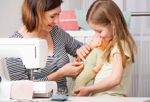Funny sewing woman doing measurements on mannequin doll with kid