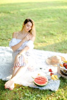 Young girl having picnic on plaid and sitting in park with fruits. Concept of resting in ope air, leisure time and summer season