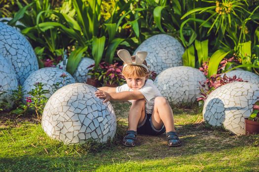 Cute little kid boy with bunny ears having fun with traditional Easter eggs hunt, outdoors. Celebrating Easter holiday. Toddler finding, colorful eggs.