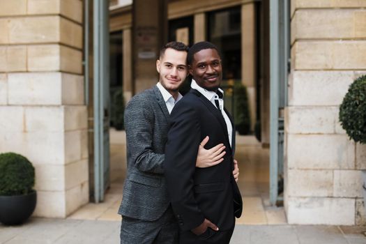 Caucasian man hugging afro american guy outside and wearing suit. Concept of happy same sex couple and lgbt gays.