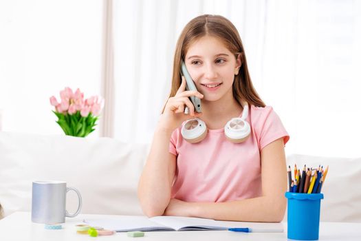 Adorable girl making calls to her school friends in free time
