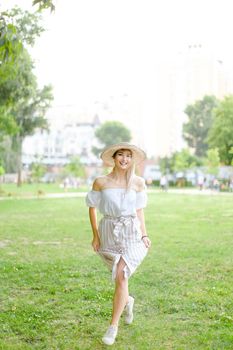 Young beautiful girl wearing hat and dress, standing in park on grass. Concept of summer season fashion and female person.