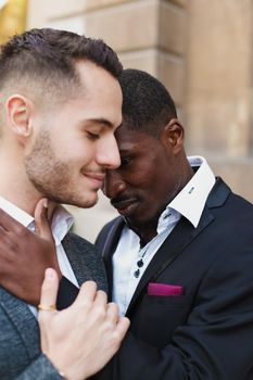 Afro american gay hugging caucasian boy outside, wearing suits. Concept of lgbt and same sex couple.