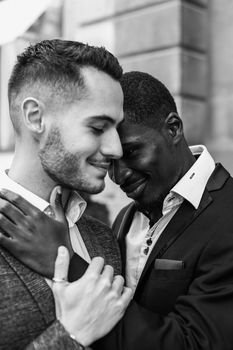 Afro american gay kissing caucasian boy outside, wearing suits. Concept of lgbt and same sex couple. Black and white bw portrait in Paris