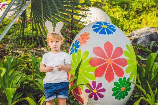 Cute little kid boy with bunny ears having fun with traditional Easter eggs hunt, outdoors. Celebrating Easter holiday. Toddler finding, colorful eggs.