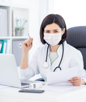 Beautiful doctor in protective mask sitting in office