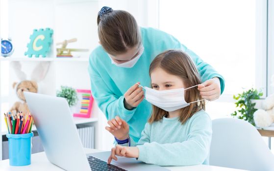 Elder sister putting on medical mask on little girl indoors