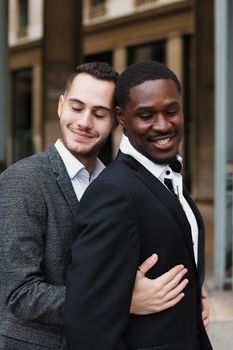 Caucasian man hugging afro american guy outside and wearing suit. Concept of happy same sex couple and lgbt gays.