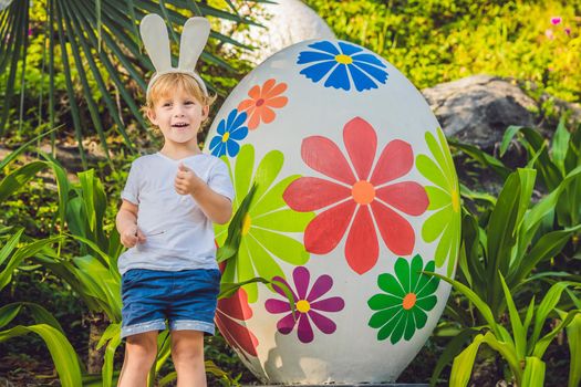 Cute little kid boy with bunny ears having fun with traditional Easter eggs hunt, outdoors. Celebrating Easter holiday. Toddler finding, colorful eggs.