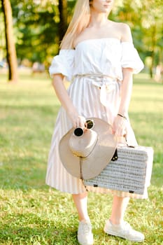 Caucasian female person standing with sunglasses and bag in garden. Concept of summer fashion and walking in park.