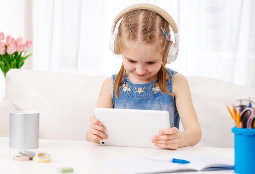 Beatiful little girl with white tablet with headphones on, in the room