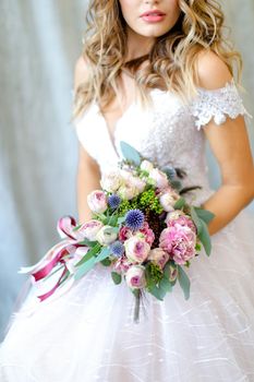 Young bride wearing white dress with bouquet at photo studio. Concept of bridal photo session, wedding and floristic art.