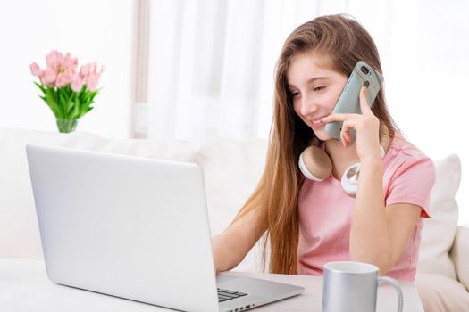 Adorable girl making calls when sitting in front of open laptop in living room