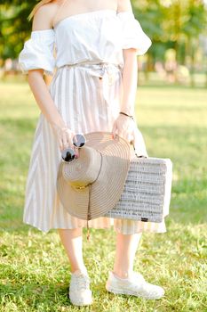 Female person standing with sunglasses and bag in garden. Concept of summer fashion and walking in park.