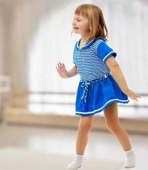 Cute little girl in a short blue dress and likes posing for the camera.In a room with a large semi-circular window.