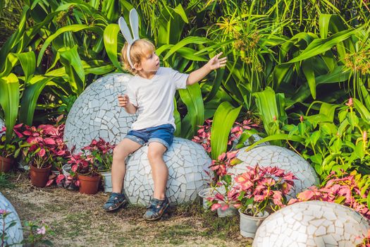 Cute little kid boy with bunny ears having fun with traditional Easter eggs hunt, outdoors. Celebrating Easter holiday. Toddler finding, colorful eggs.