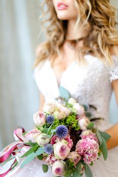 Young caucasian bride wearing white dress with bouquet at photo studio. Concept of bridal photo session, wedding and floristic art.