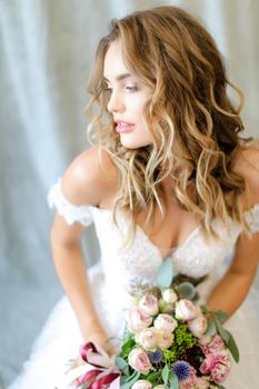 Young beautiful bride wearing white dress with bouquet at photo studio. Concept of bridal photo session, wedding and floristic art.