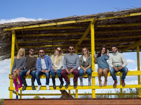 Happy Group Of Friends Hanging Out At Beach House having fun and drinking beer on autumn day