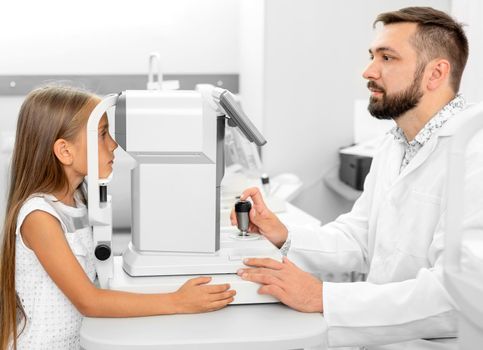 ophthalmologist holding eye equipment examinating girl's eyes in the clinic