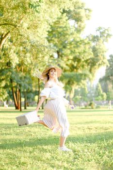 Young caucasian woman jumping in park and running, wearing fashionable clothes and hat. Concept of summer sales and style.