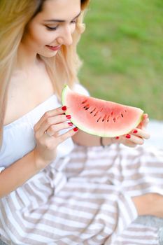 Young caucasian girl eating watermelon and wearing dress, grass in background. Concept of summer photo session, picnic.