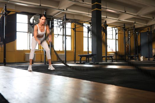 Fit woman using battle ropes during strength training at the gym