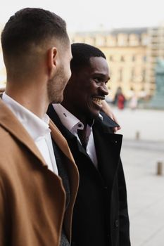 Caucasian smiling man in suit walking with afroamerican male person and hugging in city. Concept of happy lgbt gay and strolling.