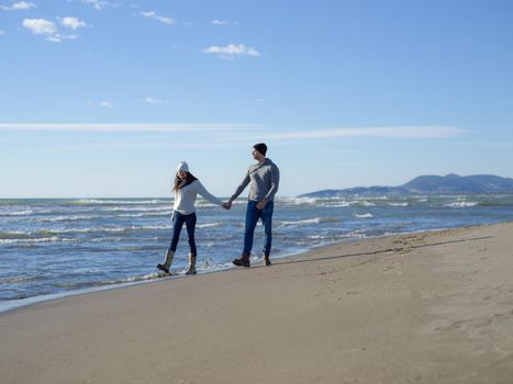 Young couple having fun walking and hugging on beach during autumn sunny day