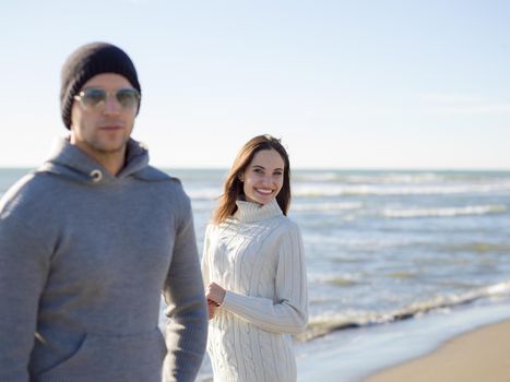 Young couple having fun walking and hugging on beach during autumn sunny day