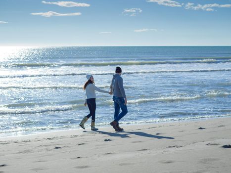 Young couple having fun walking and hugging on beach during autumn sunny day