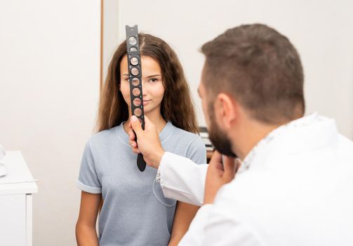 Oculist examines teenage girl with diagnostics equipment in clinic