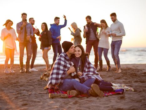 Young Couple Sitting with friends Around Campfire on The Beach At sunset drinking beer