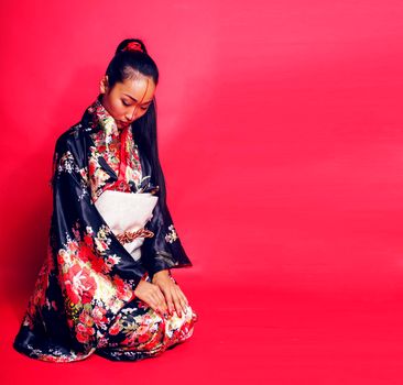 young pretty geisha on red background posing in kimono, oriental