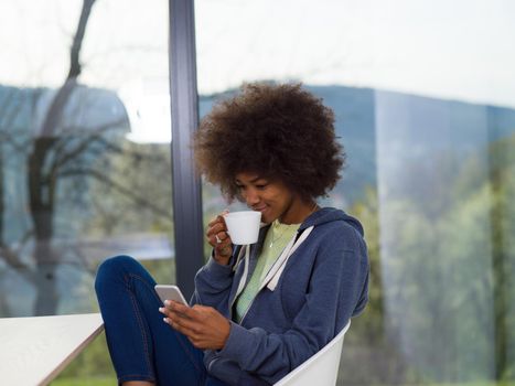 Handsome young african american woman drinking coffee and using a mobile phone at  home