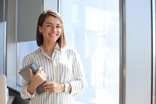 Attractive business woman looking at camera and smiling while standing in the office