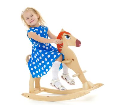 Little girl swinging on a wooden horse. The concept of a happy childhood, games in kindergarten and in the family. Isolated against white background.