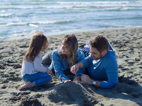 Family with little daughter resting and having fun at beach during autumn day