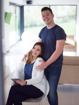 Young couple using tablet computer at luxury home together, looking at screen, smiling.