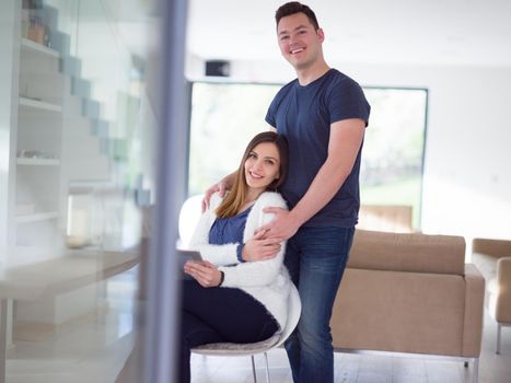 Young couple using tablet computer at luxury home together, looking at screen, smiling.